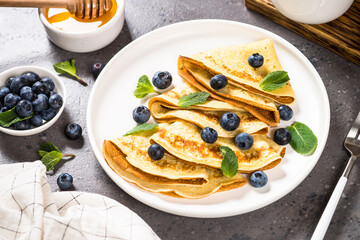 Crepes with blueberries and honey at kitchen table. Healthy breakfast or snack.