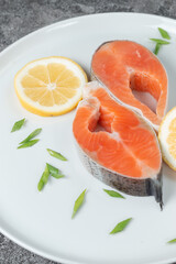 Juicy fresh salmon steak in a white plate on a wooden cutting board with onion, lemon and spices on a natural slate stone table, close-up. Deliciously cooked salmon fillet...