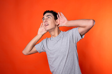 The young guy overhears and is surprised. Orange background. Blue jacket. Emotions and feelings.