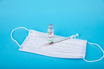 Facial medical mask and ampoule with Covid-19 vaccine on blue background to fight the coronavirus, sars-cov-2.