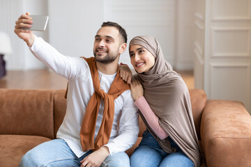 Happy Muslim Couple Making Selfie On Smartphone Sitting At Home