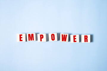 Empower word written on wood block on blue .
