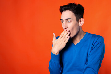 The young guy overhears and is surprised. Orange background. Blue jacket. Emotions and feelings.