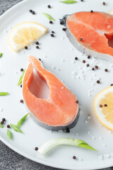Juicy fresh salmon steak in a white plate on a wooden cutting board with onion, lemon and spices on a natural slate stone table, close-up. Deliciously cooked salmon fillet...