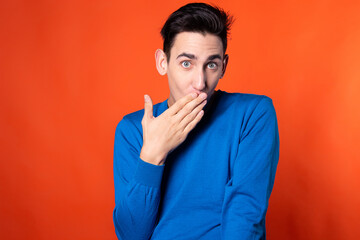 The young guy overhears and is surprised. Orange background. Blue jacket. Emotions and feelings.