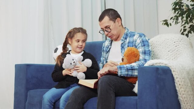 daddy read a book to her daughter at home. dream kid coronavirus stay home concept. daddy is sitting on the couch lockdown with her daughter read a book. father and daughter happy family