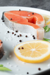 Juicy fresh salmon steak in a white plate on a wooden cutting board with onion, lemon and spices on a natural slate stone table, close-up. Deliciously cooked salmon fillet...