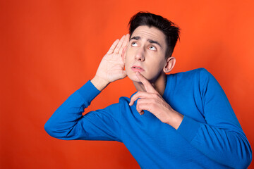 The young guy overhears and is surprised. Orange background. Blue jacket. Emotions and feelings.