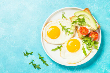 Breakfast. Fried egg, toast with white cheese and avocado and fresh salad. Healthy food. Top view with copy space at blue table.
