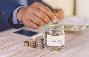 A business man's hand puts a coin in a glass bottle on the table Money saving ideas saving money for the future