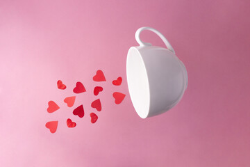 Obraz na płótnie Canvas Red hearts flying out of a white cup on a pink background.