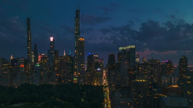Day transitions to night, aerial sliding shoot of New York City at blue hour, with avenues crossing the city from one side to another.