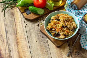 Bulgur with turkey and prunes is served with fresh vegetable on a rustic table. Copy space.