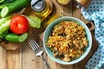Bulgur with turkey and prunes is served with fresh vegetable on a rustic table. Top view flat lay.
