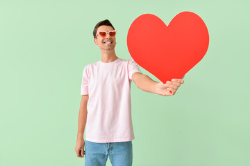 Handsome man with big red heart on color background