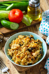 Bulgur with turkey and prunes is served with fresh vegetable on a rustic table.