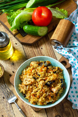 Bulgur with turkey and prunes is served with fresh vegetable salad on a rustic table.