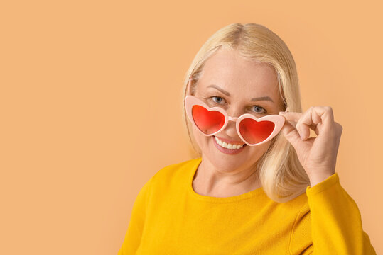 Mature woman wearing heart-shaped glasses on color background