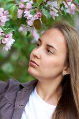 Beautiful young woman looks at a blooming apple tree in the park