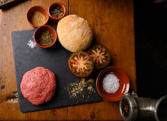 Plano de la elaboración de receta casera de hamburguesa con carne fresca cruda de ternera, especias, tomate, pan y herramientas de cocina