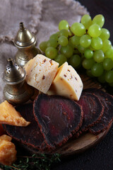 Craft cheese and green grapes on a wooden board. The sliced meat . Natural products. Wooden boards for serving food. Vertical photo on a black background.Vintage tableware.