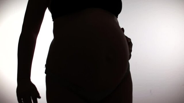 Silhouette of a large belly of a pregnant woman in an antenatal clinic. She is spinning in place, posing on a white background. The last trimester of pregnancy.