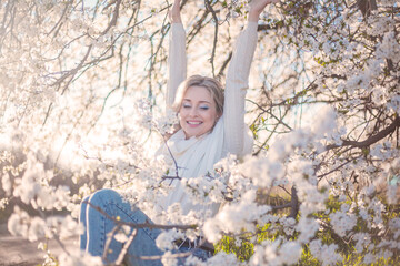 Portrait of pretty blong girl posing against the spring flowers. Woman enjoy the healthy aroma smelling in the garden