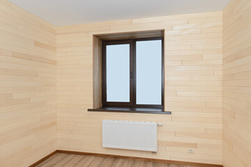 The interior of the room with a window and a radiator is covered with wooden panels