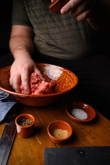 Persona elaborando una receta casera con carne cruda, especias, tomate y pan en un recipiente de barro