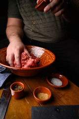 Persona elaborando receta casera con carne cruda y especias sal, pimienta
