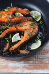 Juicy grilled salmon steak with lemon, spices and lime in a skillet on a light wooden table. Deliciously cooked salmon fillet