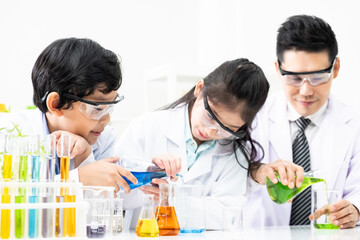 Young Asian kids wearing white scientist gown and do chemical test tube while study, learning in science classroom with teacher. Young children education concept by experiment, fun and enjoy classroom