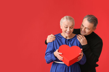 Mature couple with gift on color background. Valentine's Day celebration