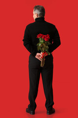 Mature man with bouquet of beautiful roses on color background