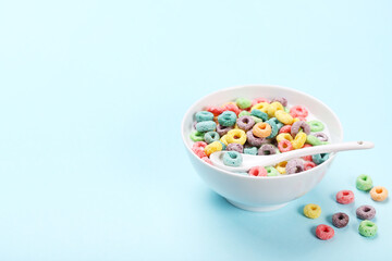 Colorful corn rings in bowl with milk and spoon on blue background