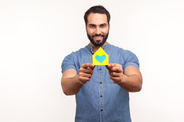 Positive bearded man holding in hands and showing paper model of house of his dream, real estate agency advertisement