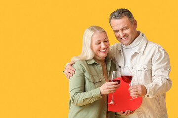 Mature couple with gift box and wine on color background. Valentine's Day celebration