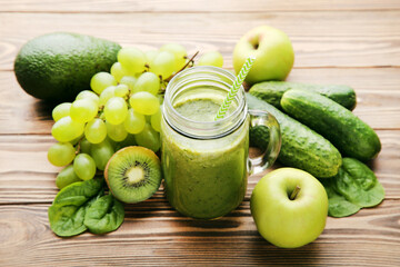 Green smoothie in glass jar with fruits and vegetables on brpwn wooden background