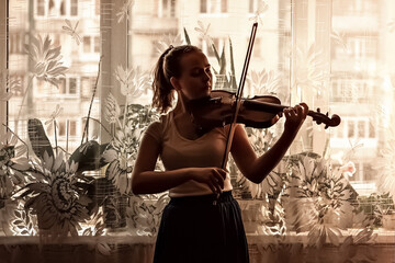 Silhouette of a young girl, a musician. Playing the violin in the background of the window