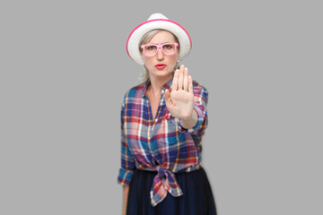 Stop or wait. Portrait of angry or scared modern stylish mature woman in casual style with hat and eyeglasses standing with stop hand sign gesture