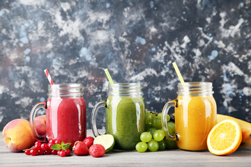 Fresh smoothies in glass jars with fruits and vegetables on wooden background