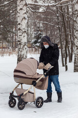 Fototapeta na wymiar Father pushing baby stroller and walking at park in blizzard. Russia