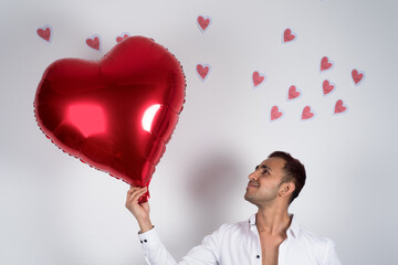 Happy man holding a red heart balloon, heart papers flying behind him, white background. love and Valentine concept 
