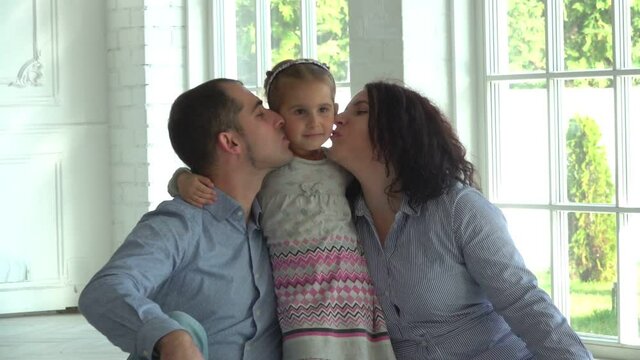 The photographer is taking pictures of parents kissing their cute little girl in a white studio