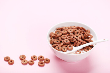Chocolate corn flakes in bowl with milk and spoon on pink background