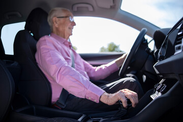 Interior Shot Of Smiling Senior Man Enjoying Driving Car With Hand On Gear Shift