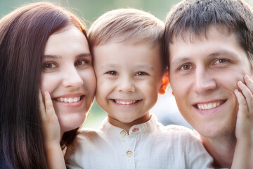 Close-up portrait of a happy young family. Mom, dad and little son look at the camera and smile. The faces of Caucasian parents and their child.