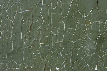 Green peeling paint on the wall. Old concrete wall with cracked flaking paint. Weathered rough painted surface with patterns of cracks and peeling. High resolution texture for background and design.