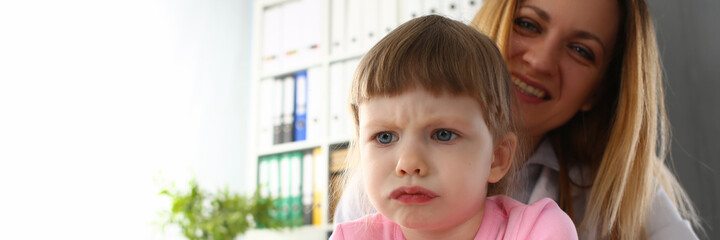 Happy young female doctor sitting with little girl during medical exam at clinic. Medicine and healtcare concept