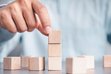 Businessman wearing a blue shirt, arranging the empty wooden blocks with his hands. Which is placed on a white wooden table. Business strategy and action plan. Copy space.